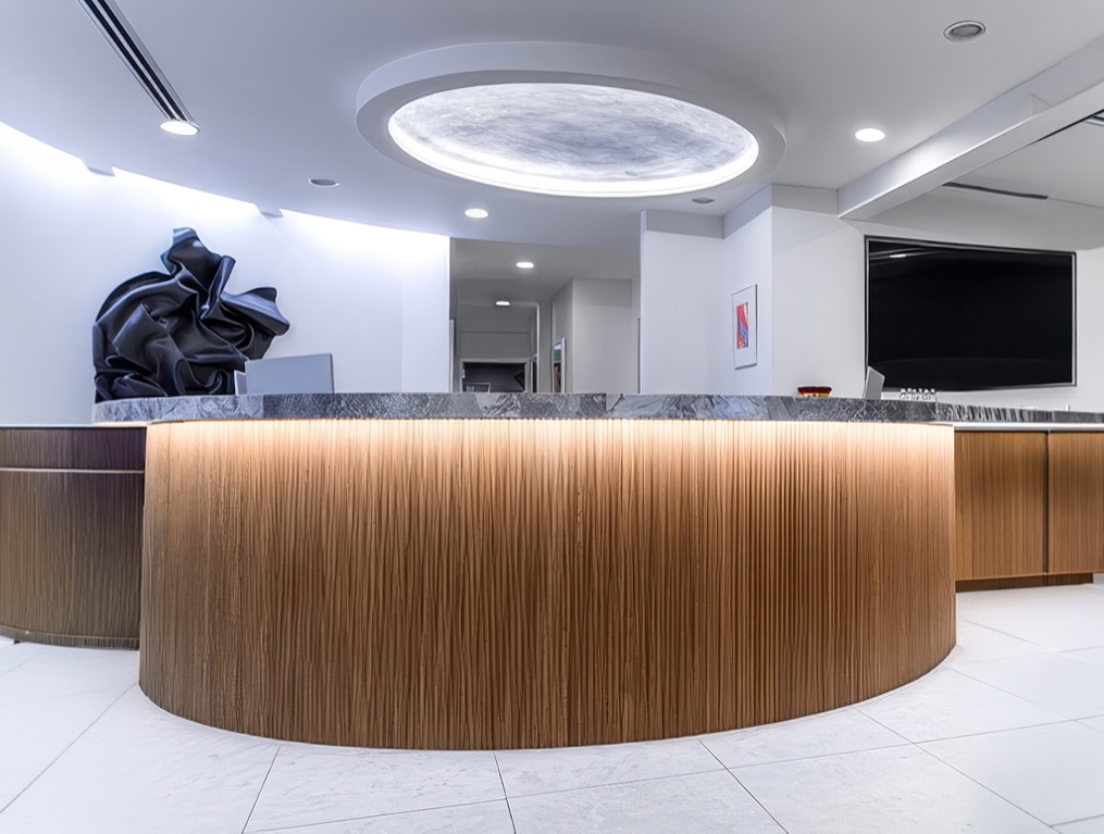 Curved wood reception desk under a circular ceiling light at the Beverly Hills office